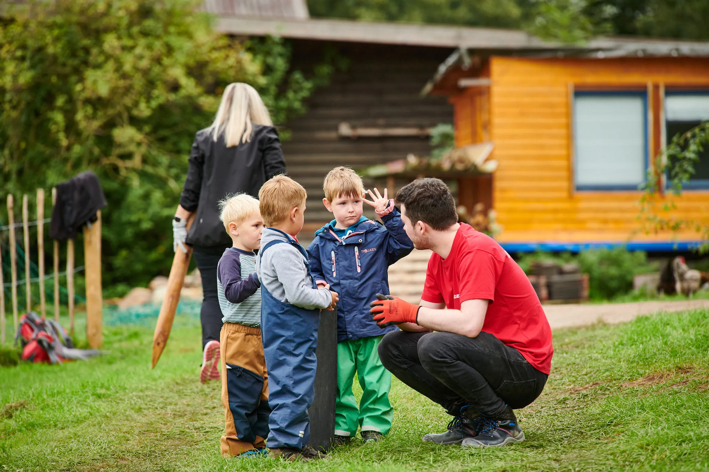 Vier Finger für vier Lebensjahre – das zeigt der kleine Junge einem Mann in rotem Hagedorn-Shirt. Gemeinsam mit zwei anderen Kindern unterhalten sie sich im Garten der Kita, während ein neuer Spielbereich gebaut wird.