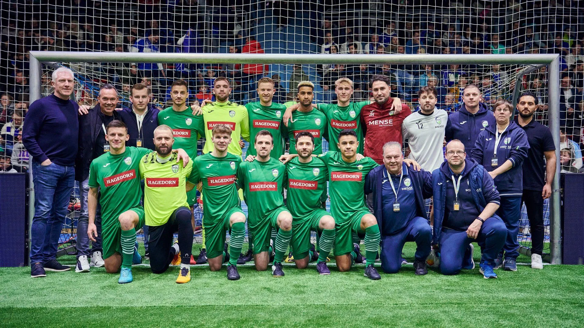 Die Mannschaft des FC Gütersloh posiert samt Trainerteam und Thomas Hagedorn im Tor der SCHWALBEarena. Die Spieler tragen stolz das Logo ihres Sponsoren „Hagedorn“ auf der Brust.